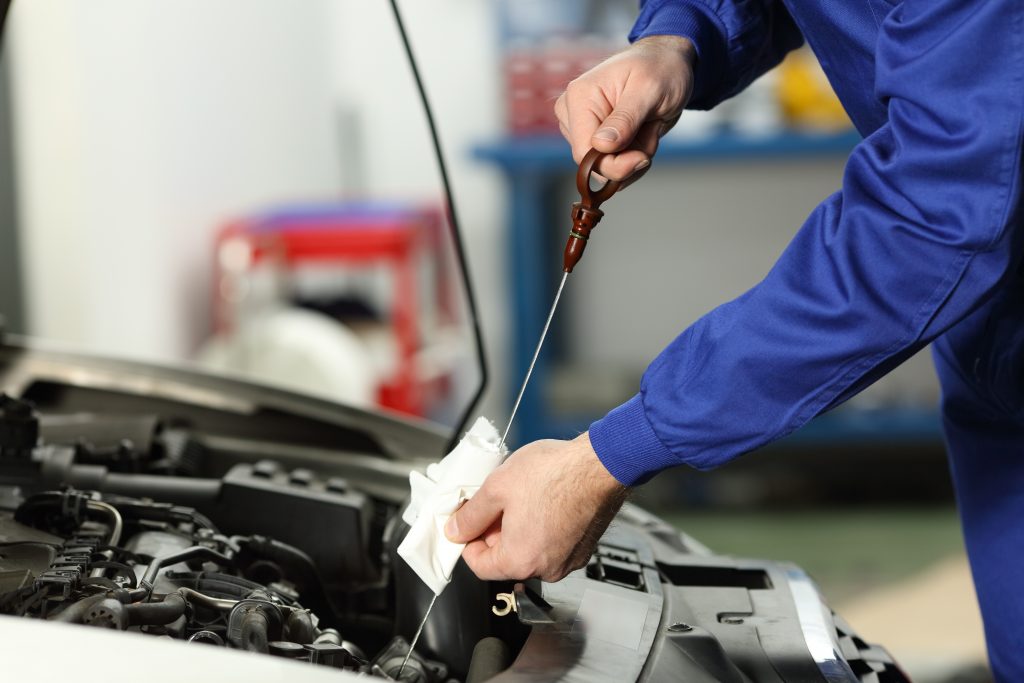 a mechanic at an oil change franchise wiping the dipstick clean with a rag, before plunging it back into its tube for an accurate oil level measurement. 